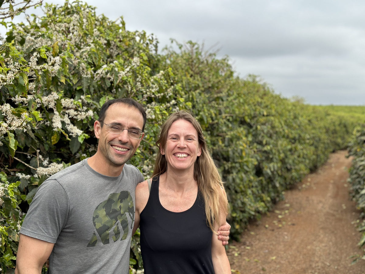 Paulo and Juliana Piancastelli standing in a flowering coffee row at Fazenda Terra Alta