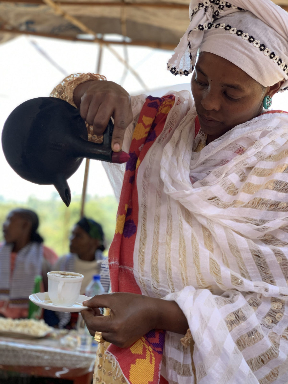Woman in traditional dress pouring coffee from a jebena into small cups
