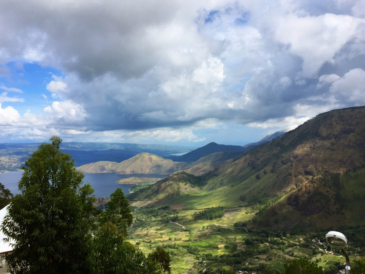 A wide view over a green highland valley down to a large lake with mountains behind